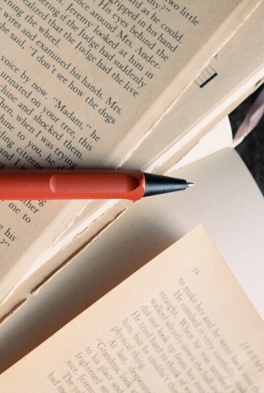 A close-up of a red-coloured pen resting on top of loose pages of English text.
